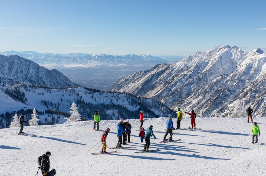 Skid- och snowboardåkare på toppen av en snöig topp med berg som sträcker sig i fjärran