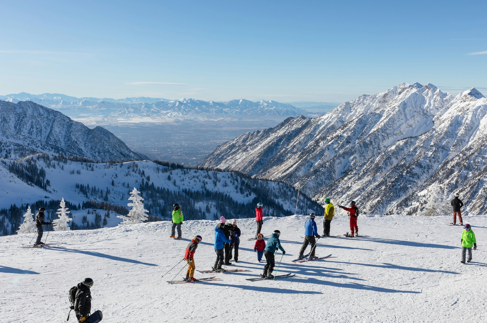 Skiers and snowboarders on top of a snowy peak with mountains stretching into the distance
