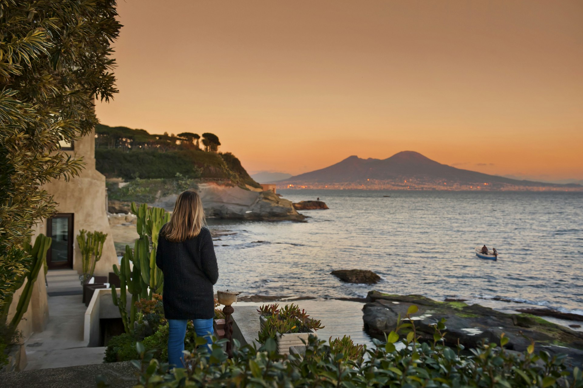 Rear view of a woman looking out over a boat in the water with Mount Vesuvius in the background