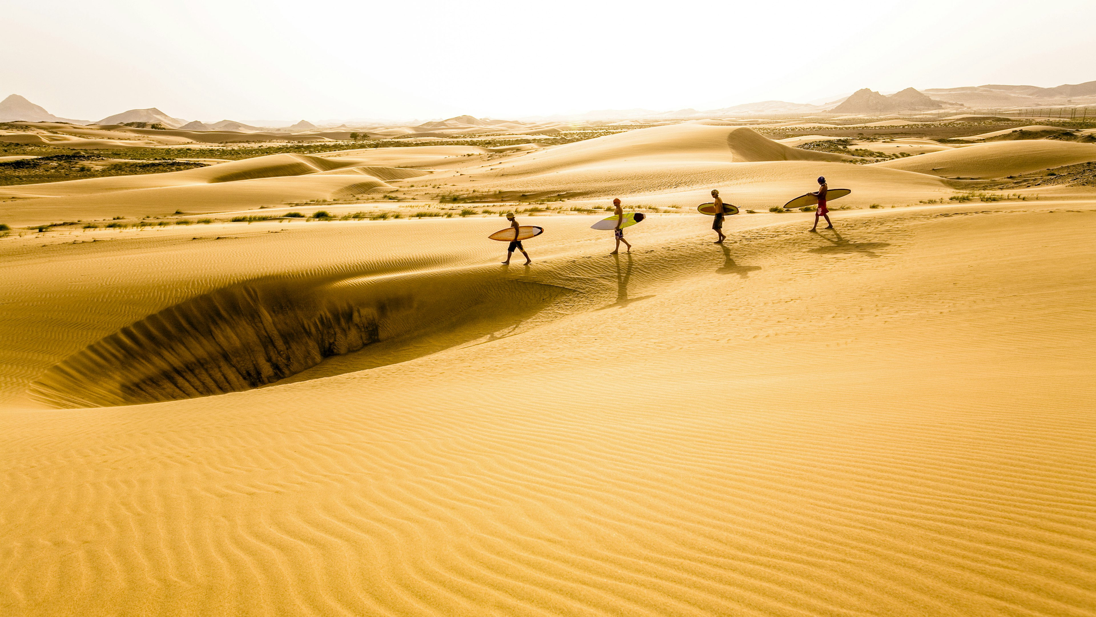 Oman, Ash Sharquiyah, four surfers walking on sand dunes in the desert