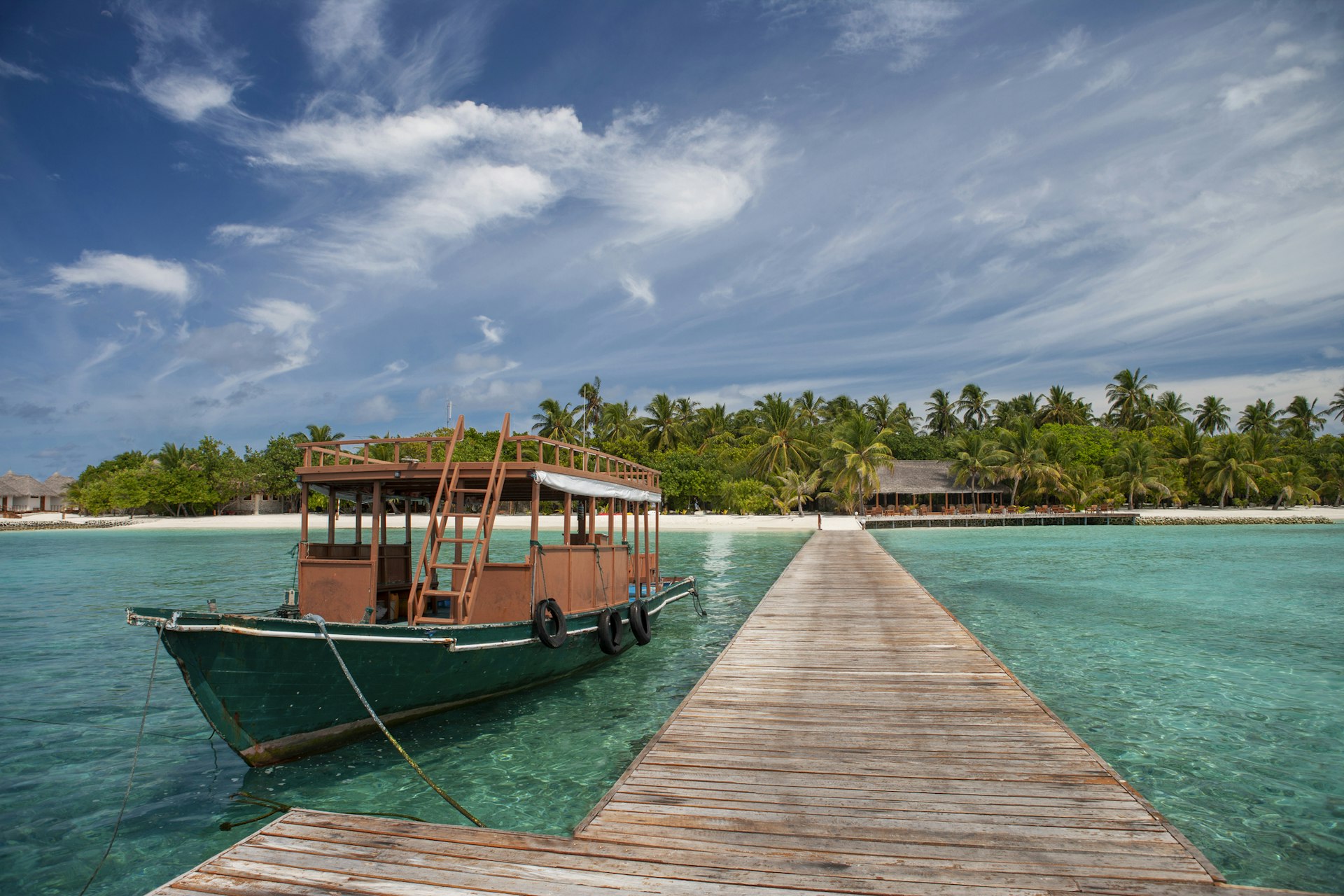 A traditional wooden boat moored next to a long pier with a tropical island in the background