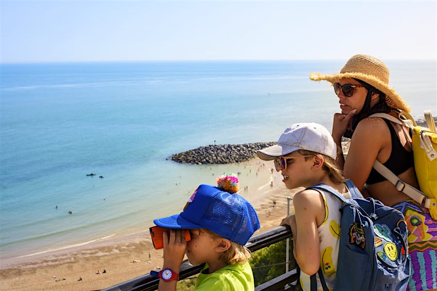 Mother and children stand on a viewpoint over a sandy beach on a sunny day