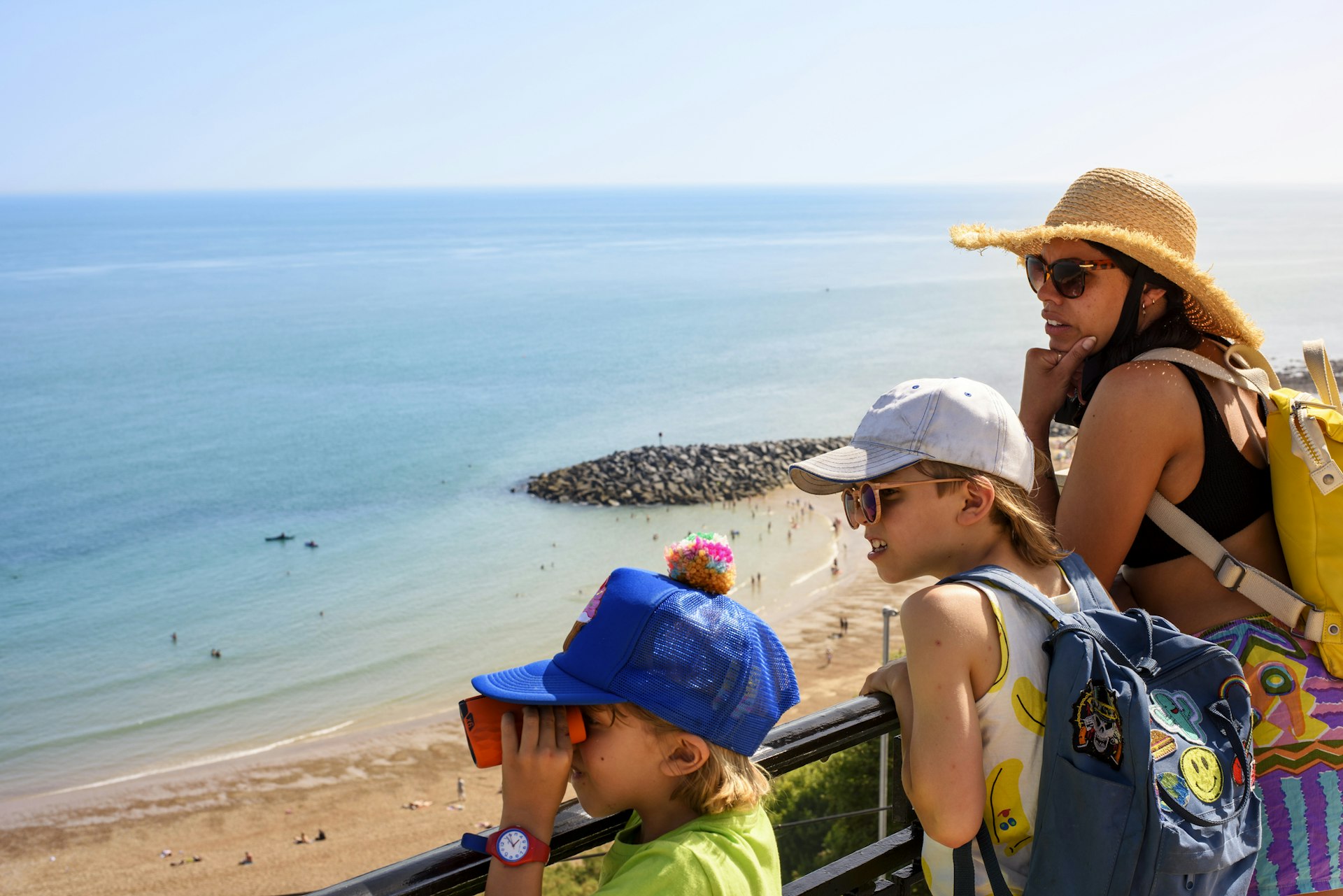 Mother and children stand on a viewpoint above a sandy beach on a sunny day