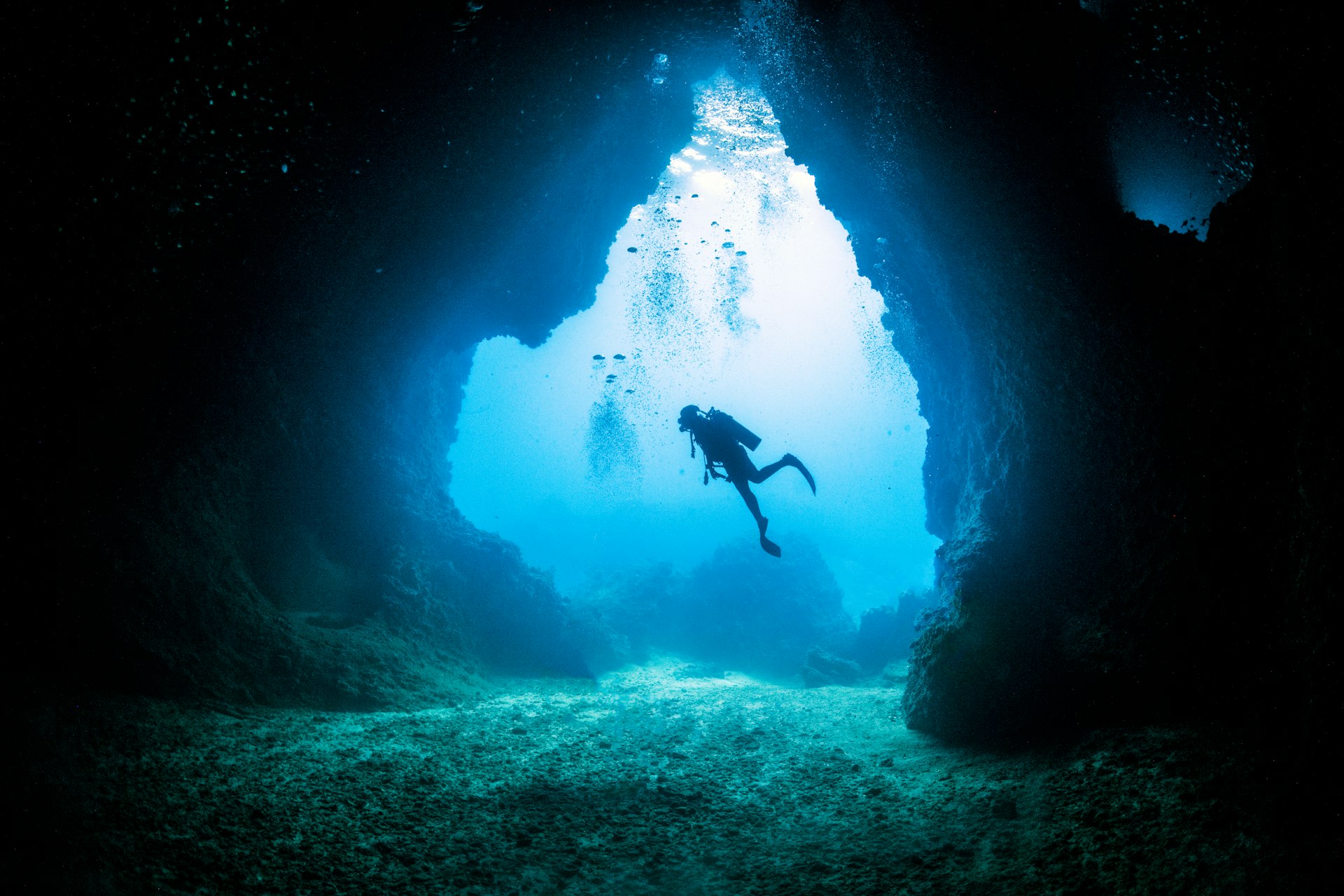 A scuba diver is in silhouette as light floods into an underwater cave