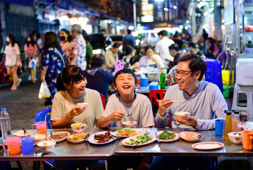 Asian family enjoy eating food on street food restaurant with crowd of people at Yaowarat road, Bangkok