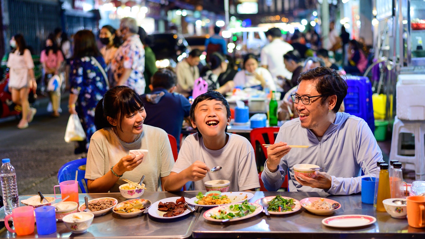 Asian family enjoy eating food on street food restaurant with crowd of people at Yaowarat road, Bangkok