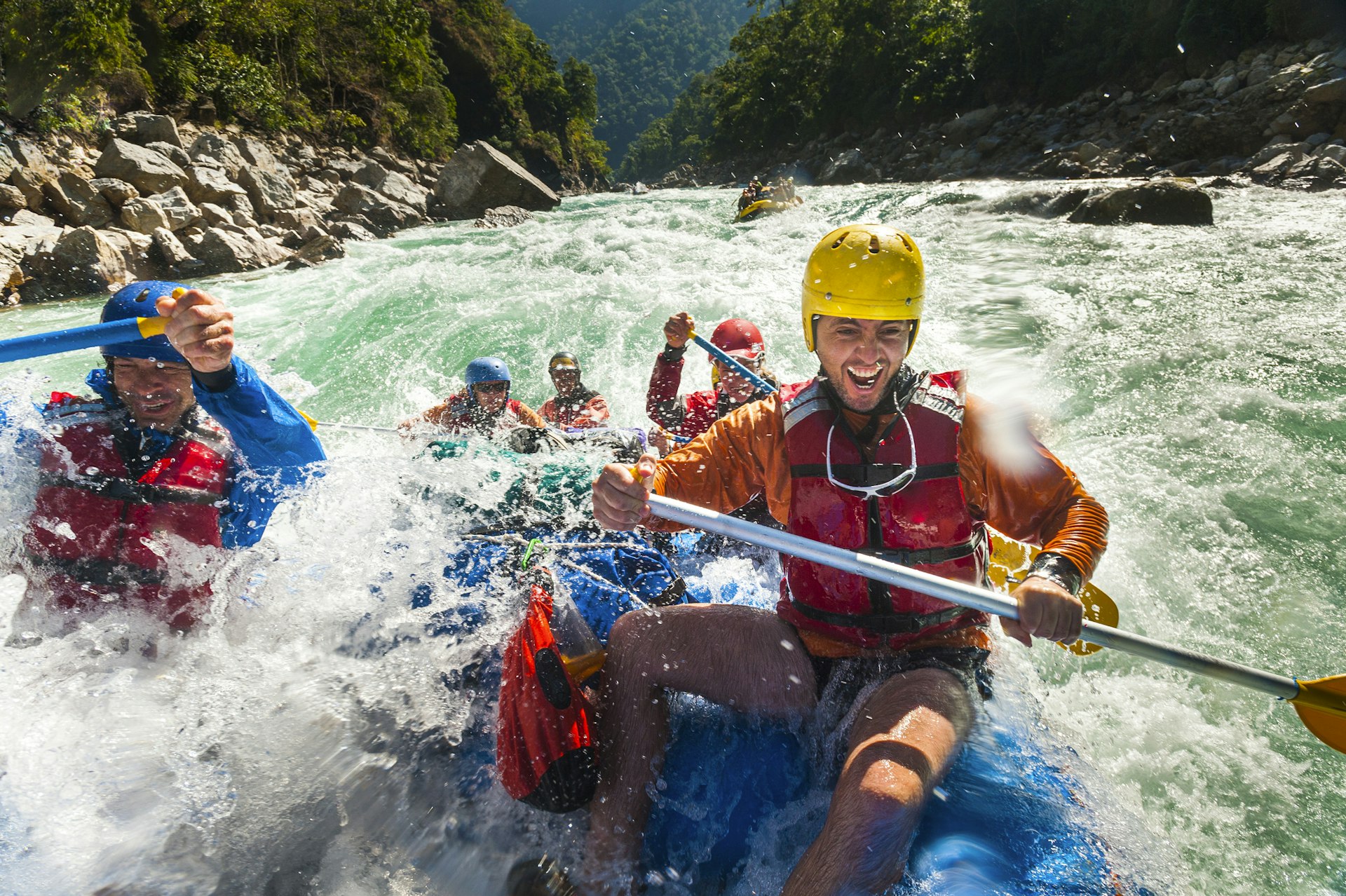 Rafters wearing safety gear and helmets get splashed as they go through some big rapids on a river 
