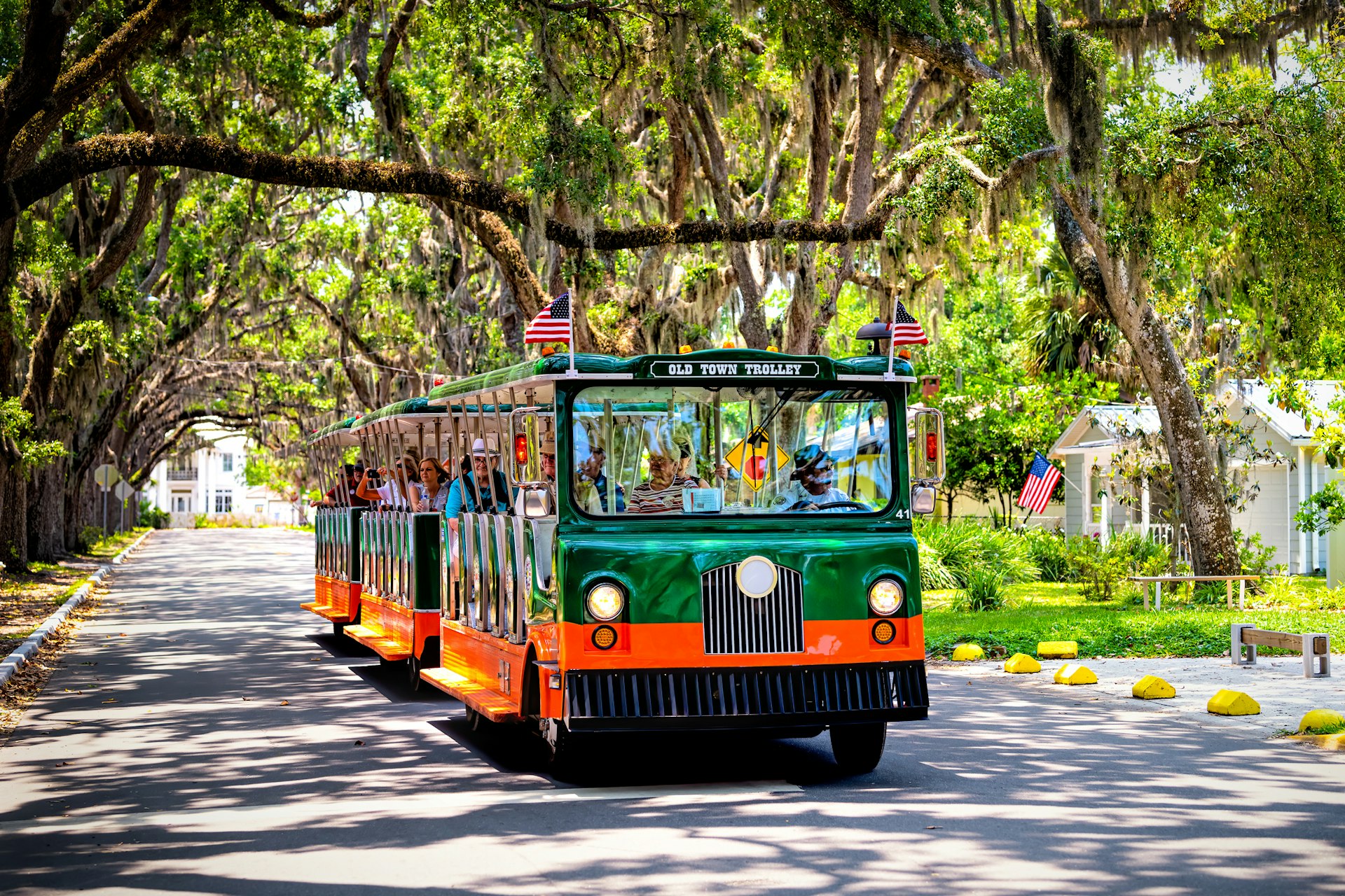 People riding on old town trolley guided tour on a road with live oak trees and a canopy of hanging Spanish moss draped over it