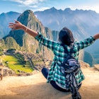 A woman tourist contemplating the amazing landscape of Machu Picchu with arms open. Archaeological site, UNESCO World Heritage