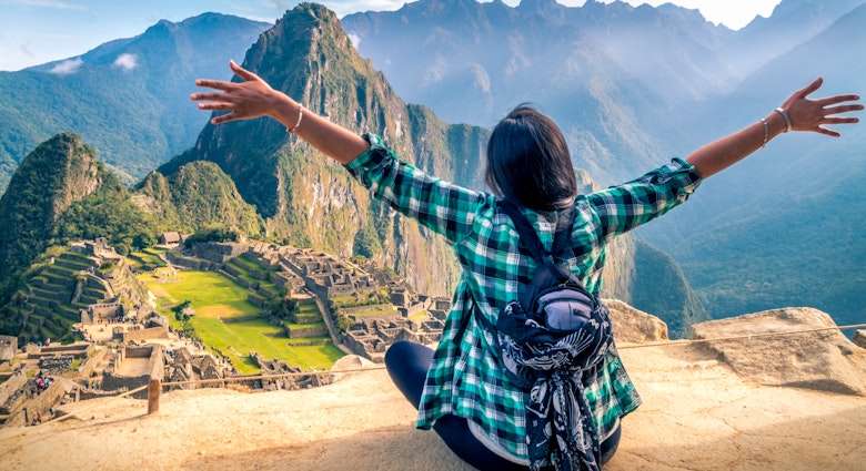 A woman tourist contemplating the amazing landscape of Machu Picchu with arms open. Archaeological site, UNESCO World Heritage