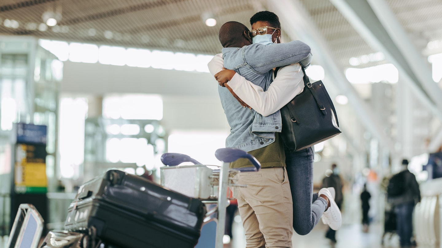 African man hugging and lifting woman at airport terminal. Couple meet after long separation at airport post pandemic lockdown.