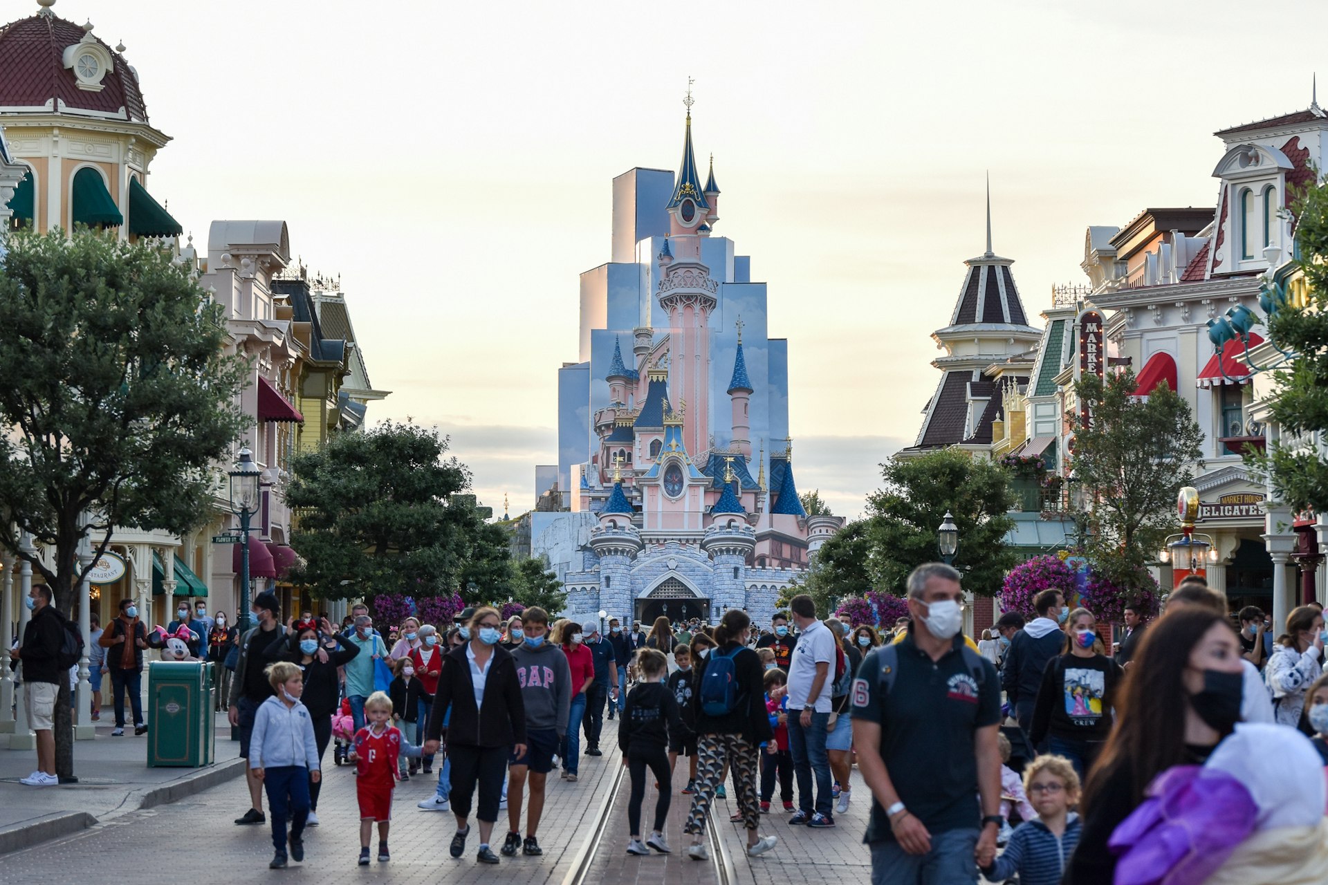 Tourists on Main Street in Disneyland Paris, with a pale pink fairy-tale castle rising above them in the distance