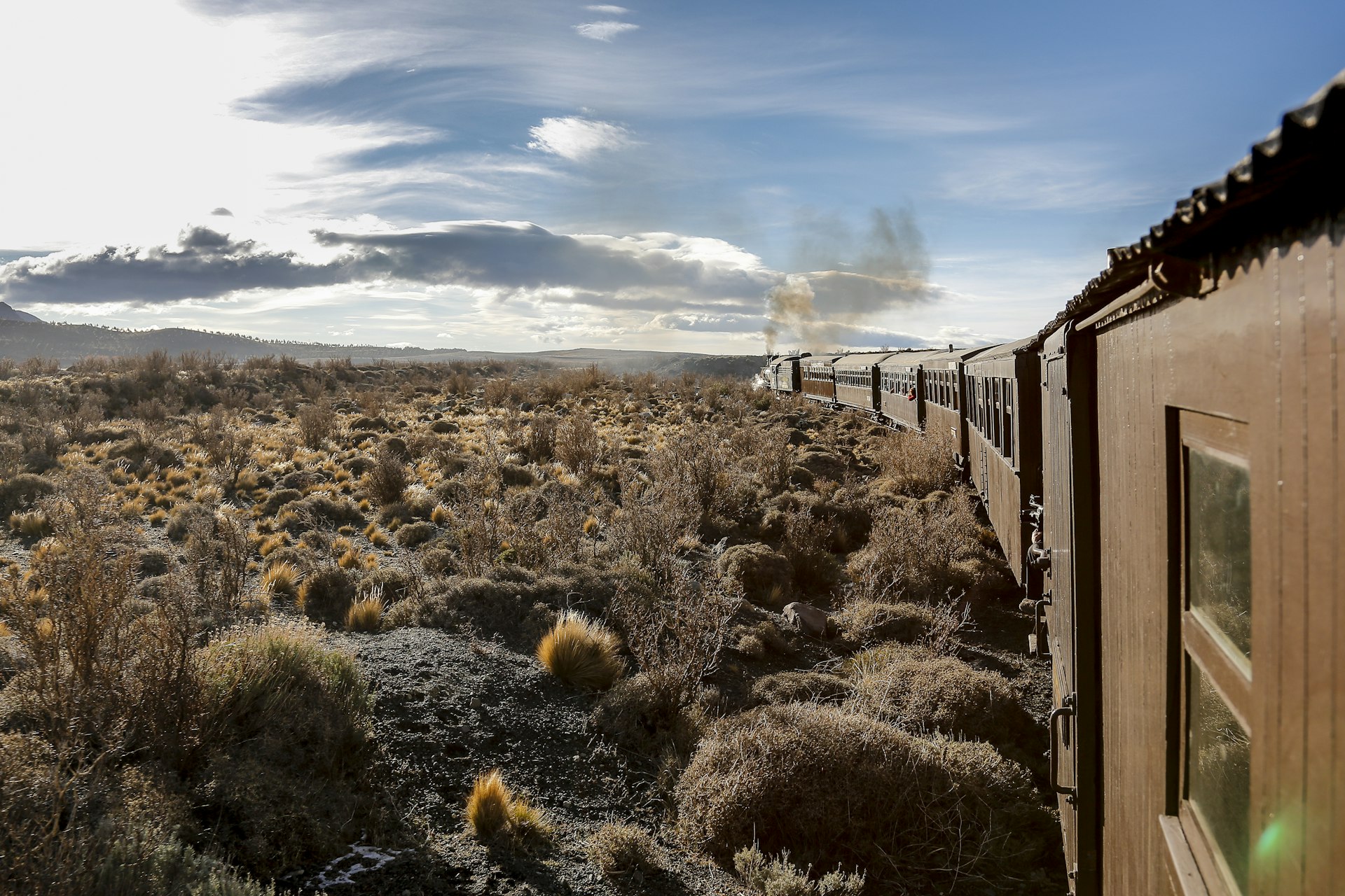 The Patagonia countryside as seen by The Old Patagonian Express steam train, which bends around to the left, curling towards the scrub and shrubs and big rocks.