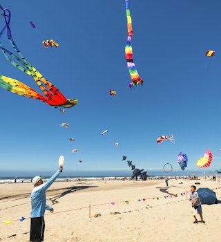 Lincoln City, Oregon,USA- June 26, 2016: Annual kite festival in Linclon City on the Oregon Coast.  A man and boy play with paddles and ball on sandy beach under a sky full of kites.