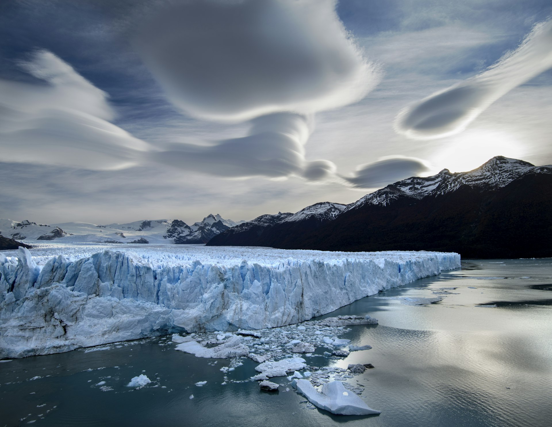 Under gray-white blob-like clouds, the Perito Moreno Glacier in Chile - a jagged blue-white mass of ice -- slowly moves in a glacial lake looking like a huge clifftop