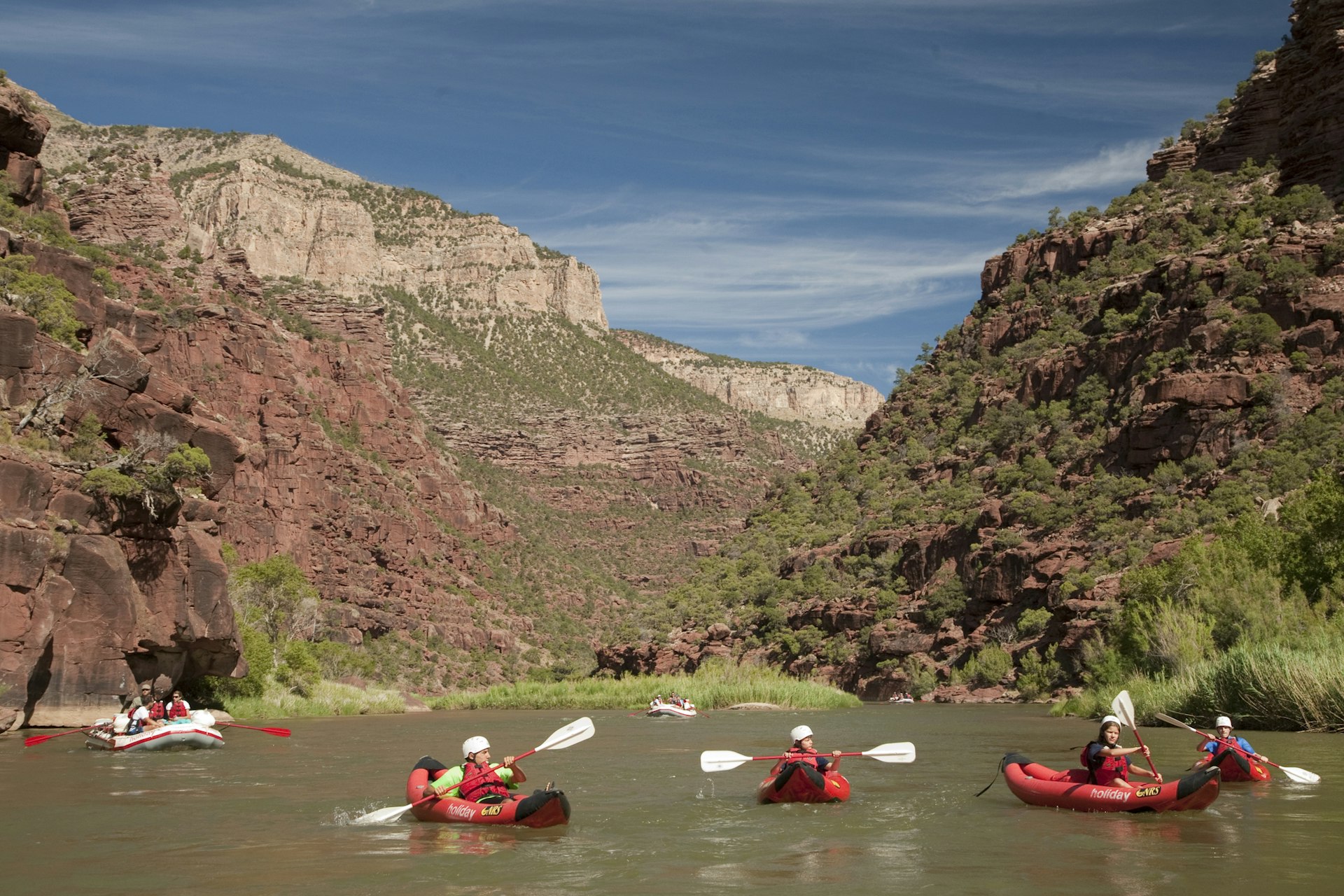 A group of people in red kayaks on a river in a gorge