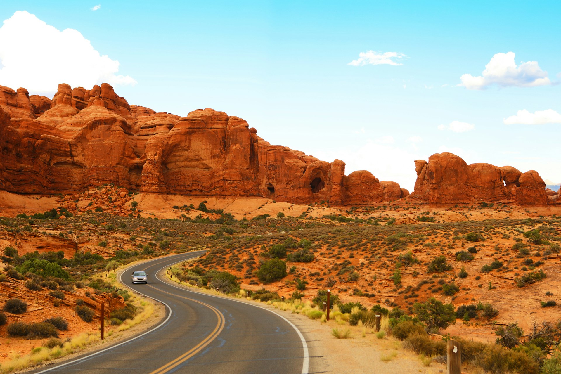A car driving on a winding road through a rural area with large red rocks dominating the sccene
