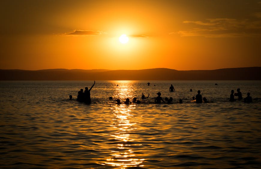 Swimmers in a lake in silhouette as the sun sets