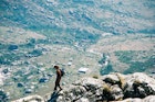 Side view of a Female hiker walking down on a mountain ridge with a day pack and the Chisepo Hut in the background below Mount Mulanje Mountain Range Mulanje Zoma Plateau Malawi Africa