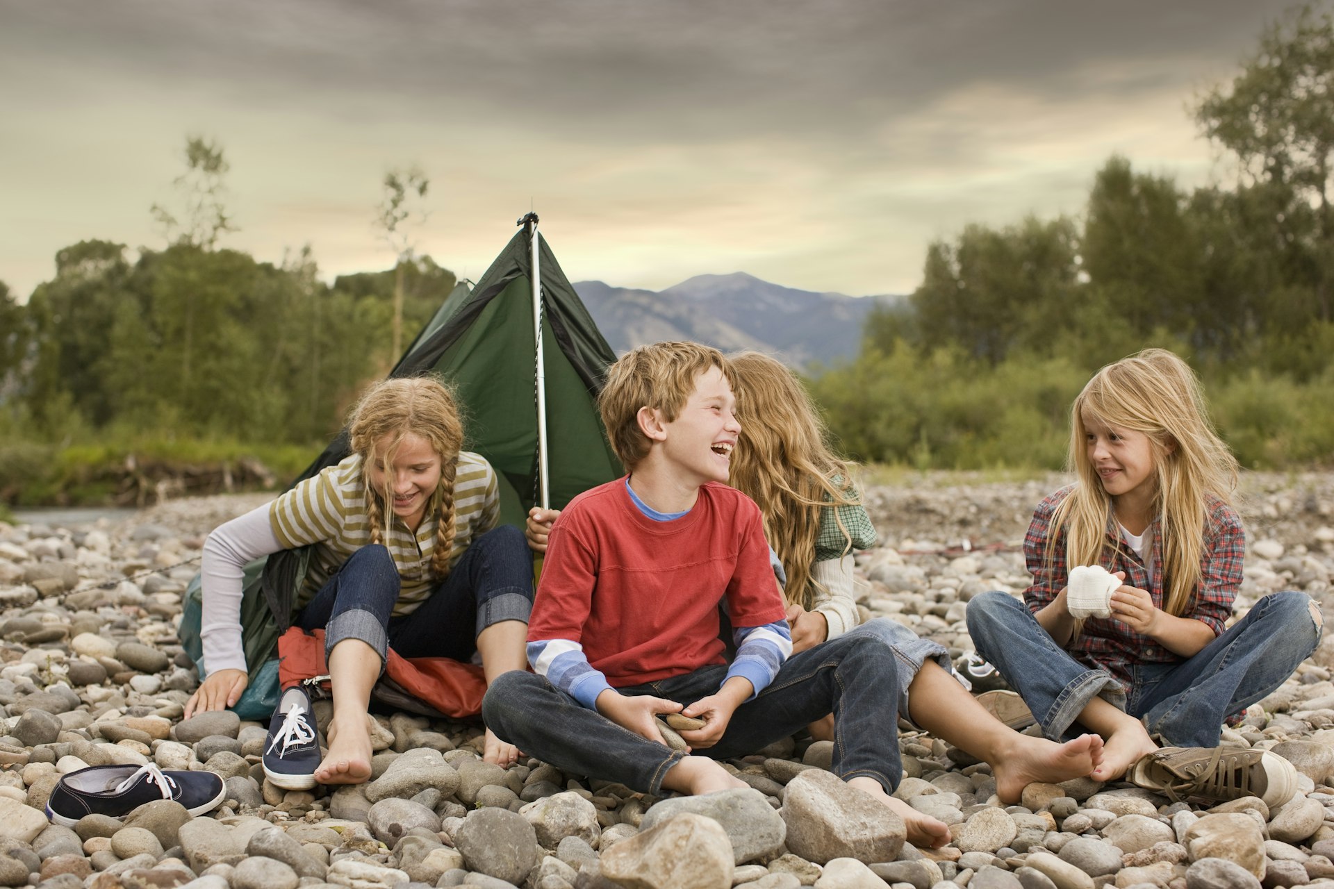 Brother and sisters playing in small tent on a rocky creek bank