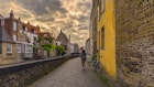 Woman Walking Alone In Bruges Against Sunrise