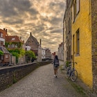 Woman Walking Alone In Bruges Against Sunrise