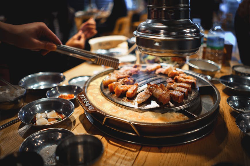 Un dîner avec des baguettes atteint pour la viande sur le gril dans un restaurant barbecue à Séoul, Corée du Sud