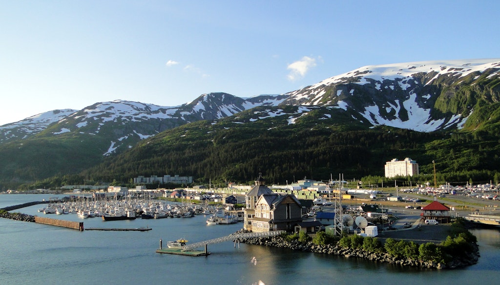 Boats in the harbor of Whittier, Alaska, with snow-fringed mountains rising behind the town