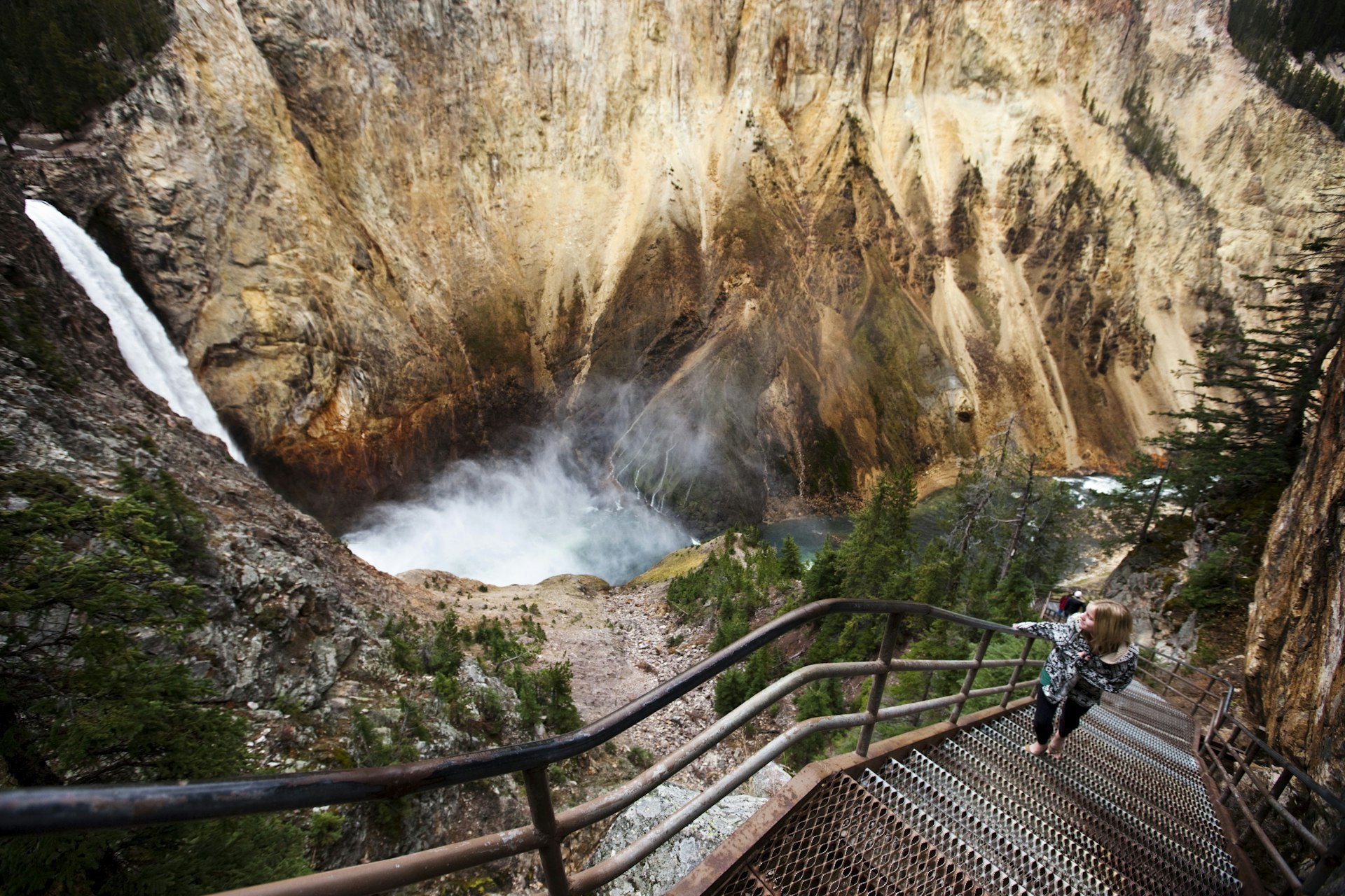 A young woman walks up a narrow staircase, winding down to an overlook of Yellowstone Falls