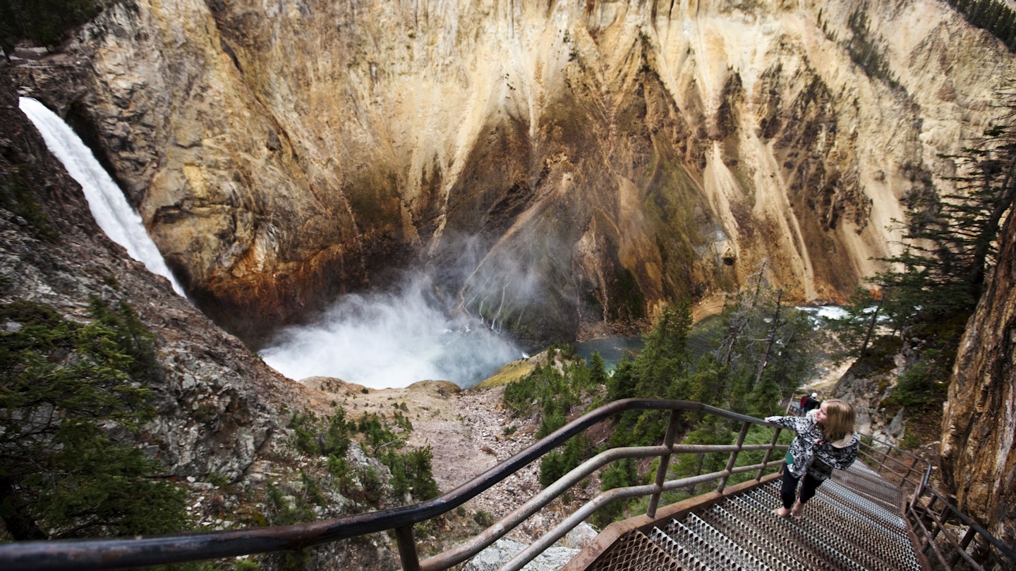 A young woman walks up a narrow stair set winds down to a overlook of Yellowstone Falls in Yellowstone National Park, Wyoming.