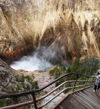 A young woman walks up a narrow stair set winds down to a overlook of Yellowstone Falls in Yellowstone National Park, Wyoming.