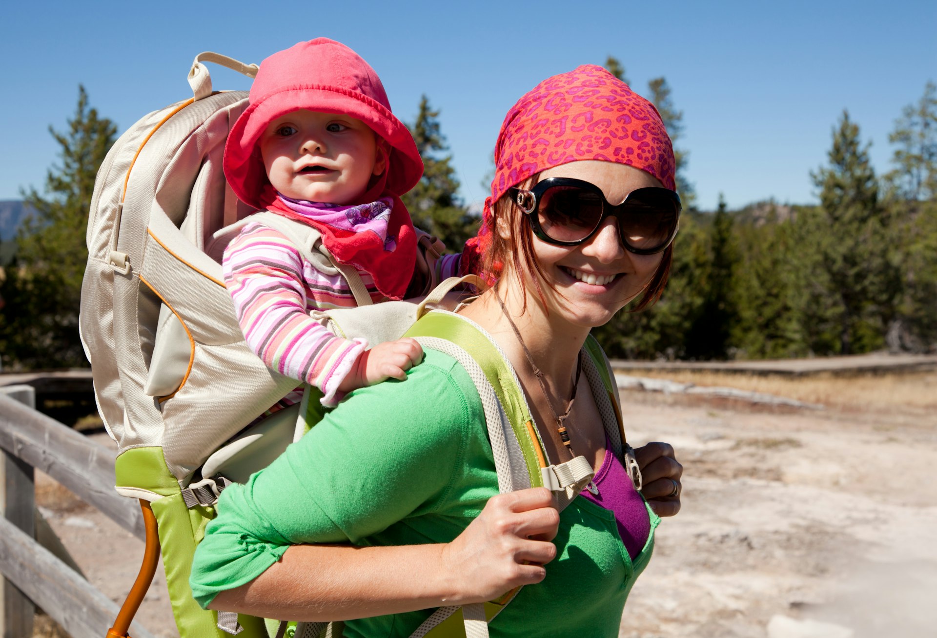 Smiling mother with her baby daughter in backpack carrier on a sunny day at Yellowstone National Park
