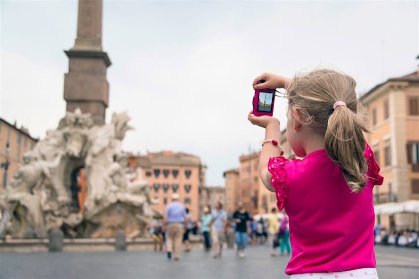 Horizontal image of a 6 year old girl in a pink shirt taking photos in Piazza Navona, Rome, Italy.
