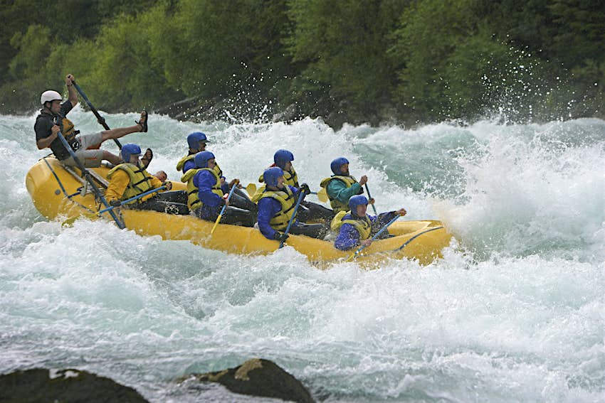 White-water rafting in Futaleufú A group of eight people in blue wetsuits, helmets and yellow lifejackets white-water raft along the Futaleufu River with the leader at the back almost being chucked from his seat