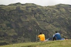 Two hikers take a food break on a grassy hill in a remote valley outside of the town of Riobamba.