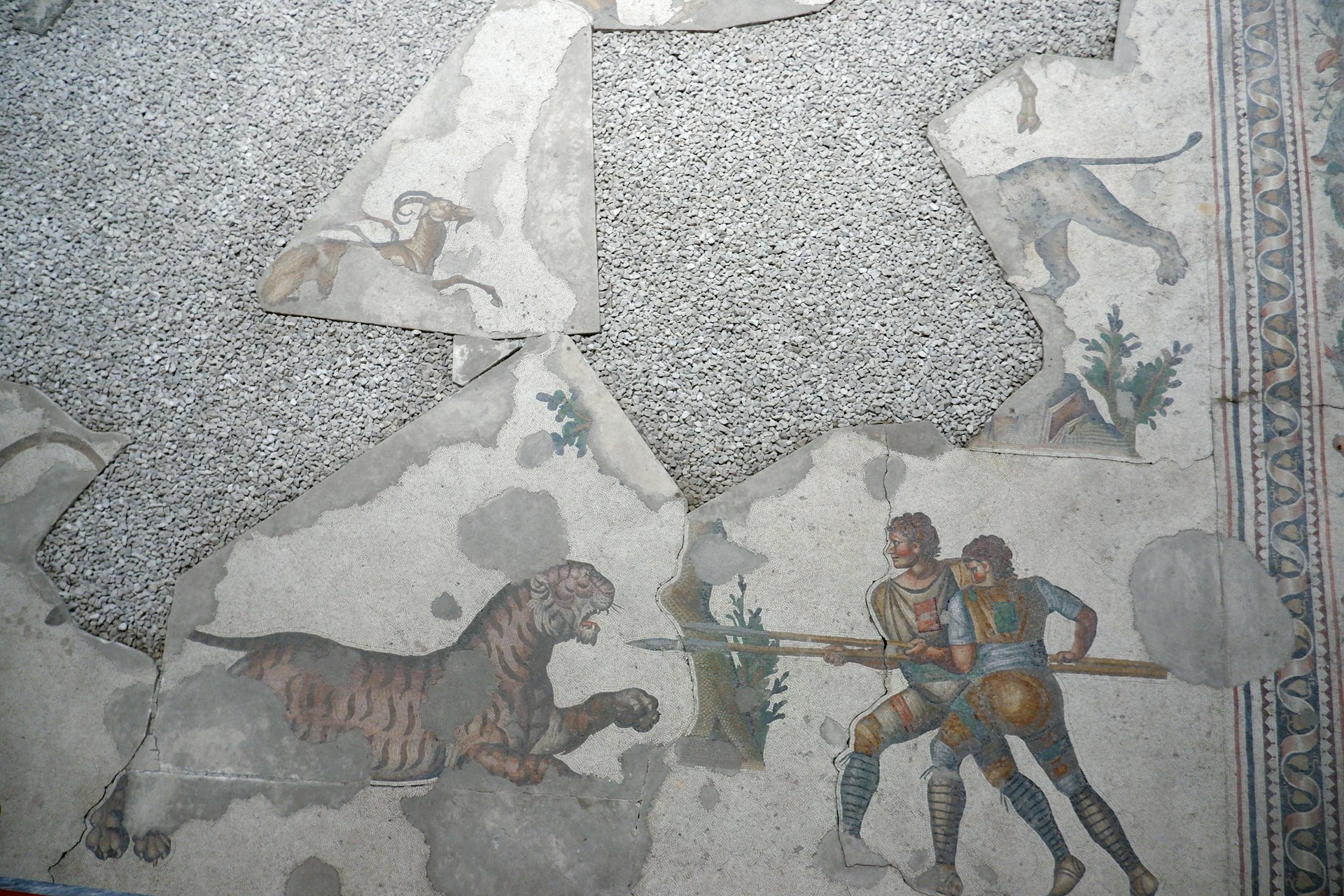 A portion of a mosaic depicting men with spears pointed toward an animal