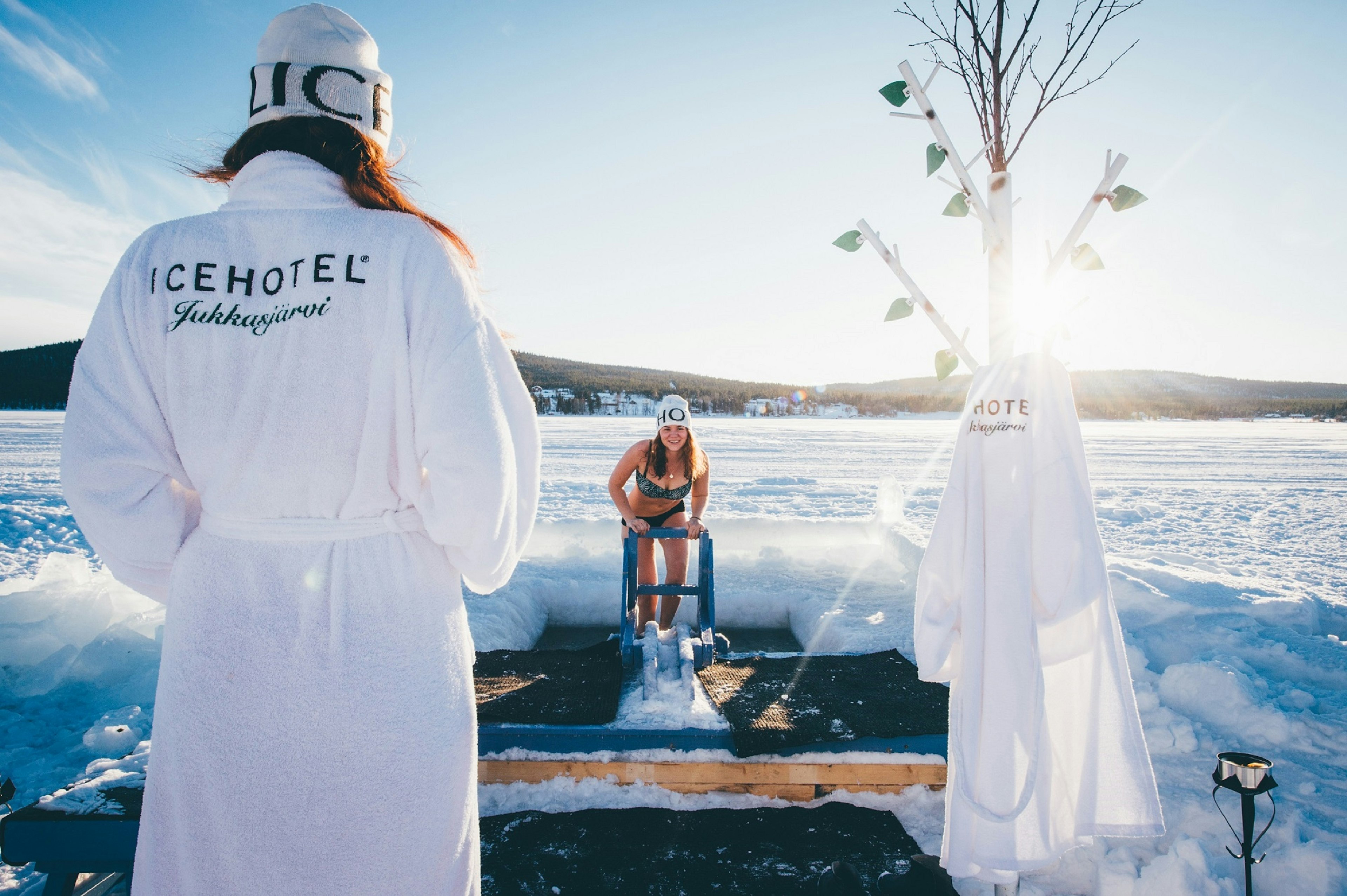 Two women in bathing suits and robes prepare to enjoy an ice-plunge pool