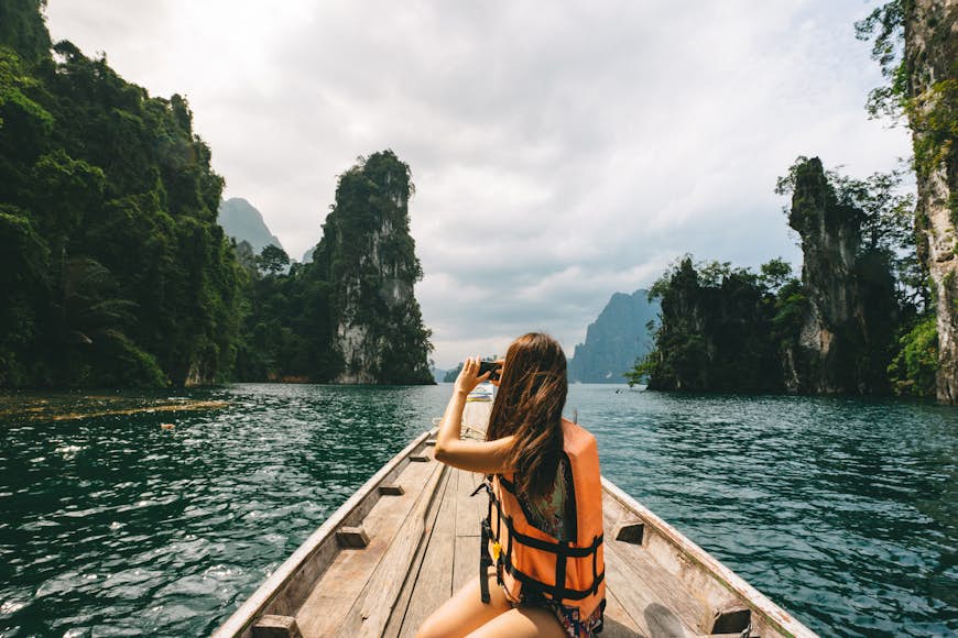 Female tourist exploring a lush lake surrounded by jungle and limestone cliffs in Khao Sok National Park