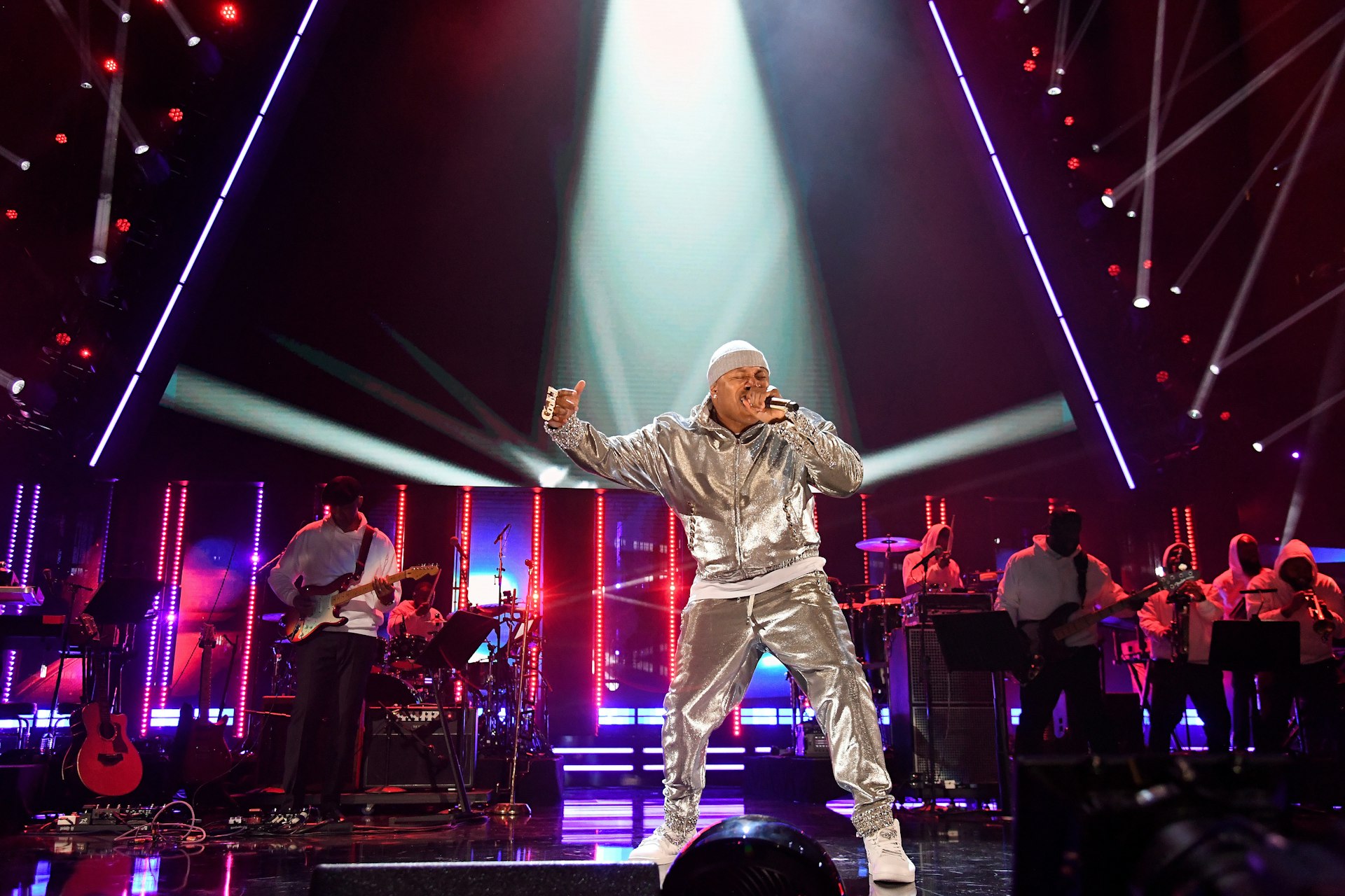 Rapper LL Cool J in a silver jogging suit performs in front of a band. 