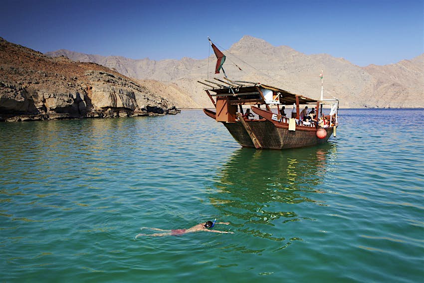 Un homme plonge près d'un bateau traditionnel dans les eaux au large de Musandam, Oman