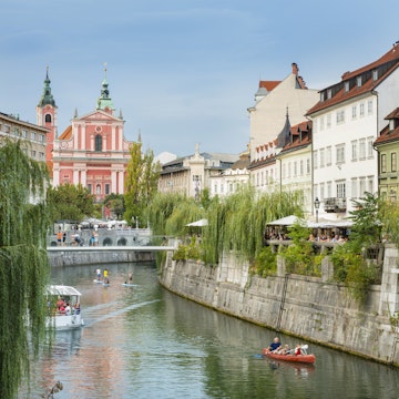 Boats and paddle boarders travel down the tree-lined Ljubljanica River, which flows through the centre of Ljubljana.