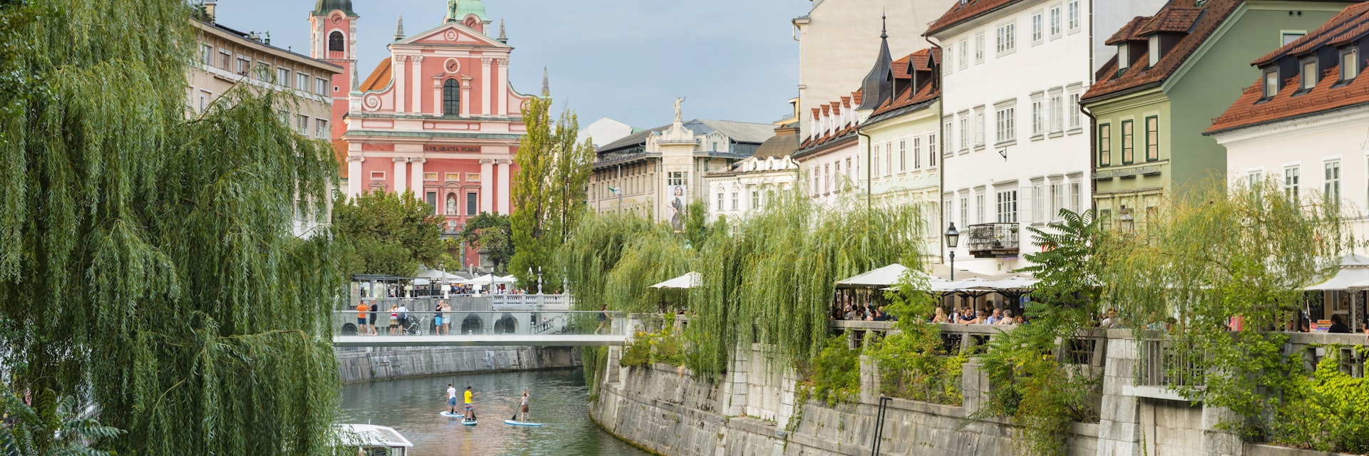Boats and paddle boarders travel down the tree-lined Ljubljanica River, which flows through the centre of Ljubljana.
