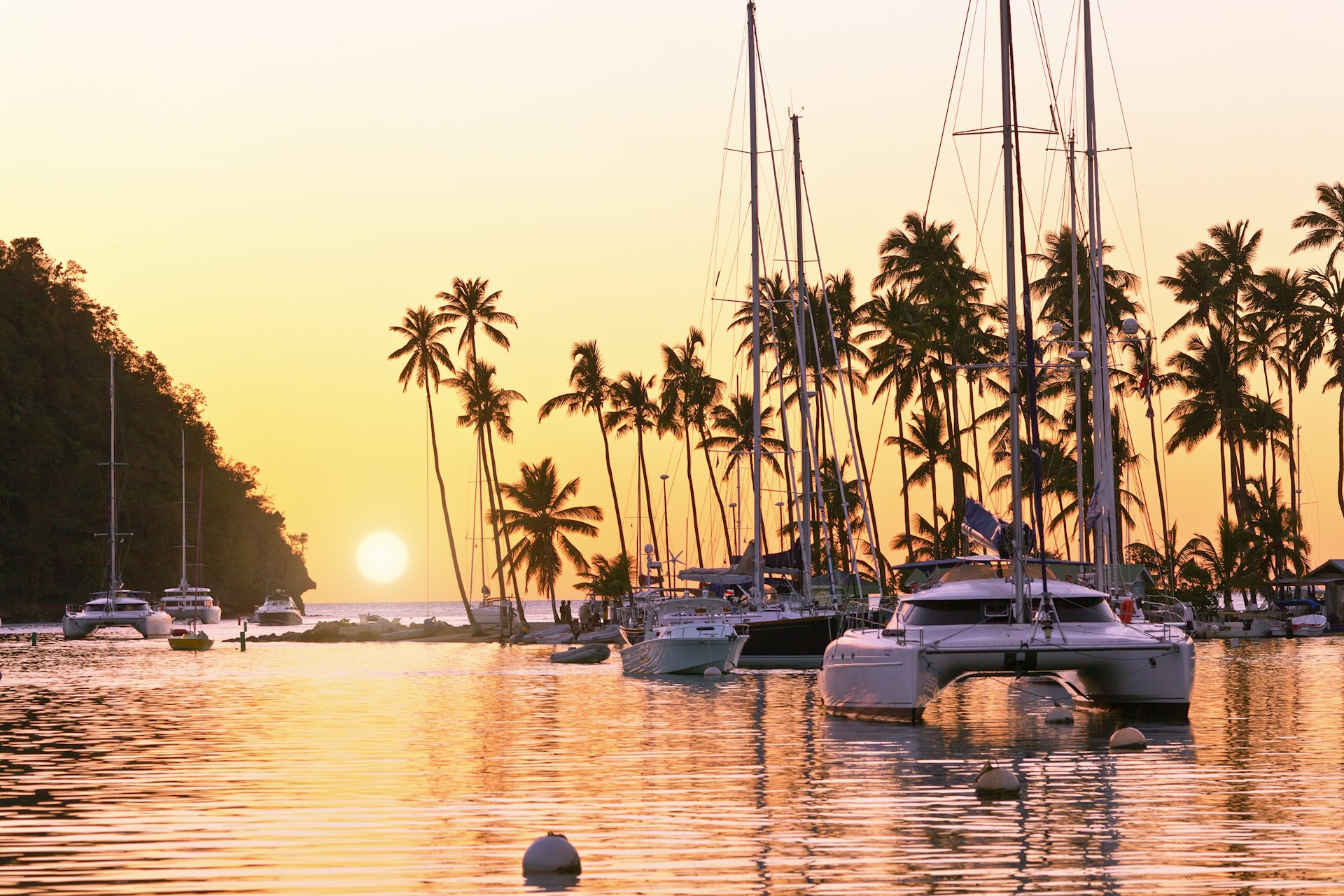 Boats sit in a peacefull bay surrounded by palm trees as the sun sets out over the sea