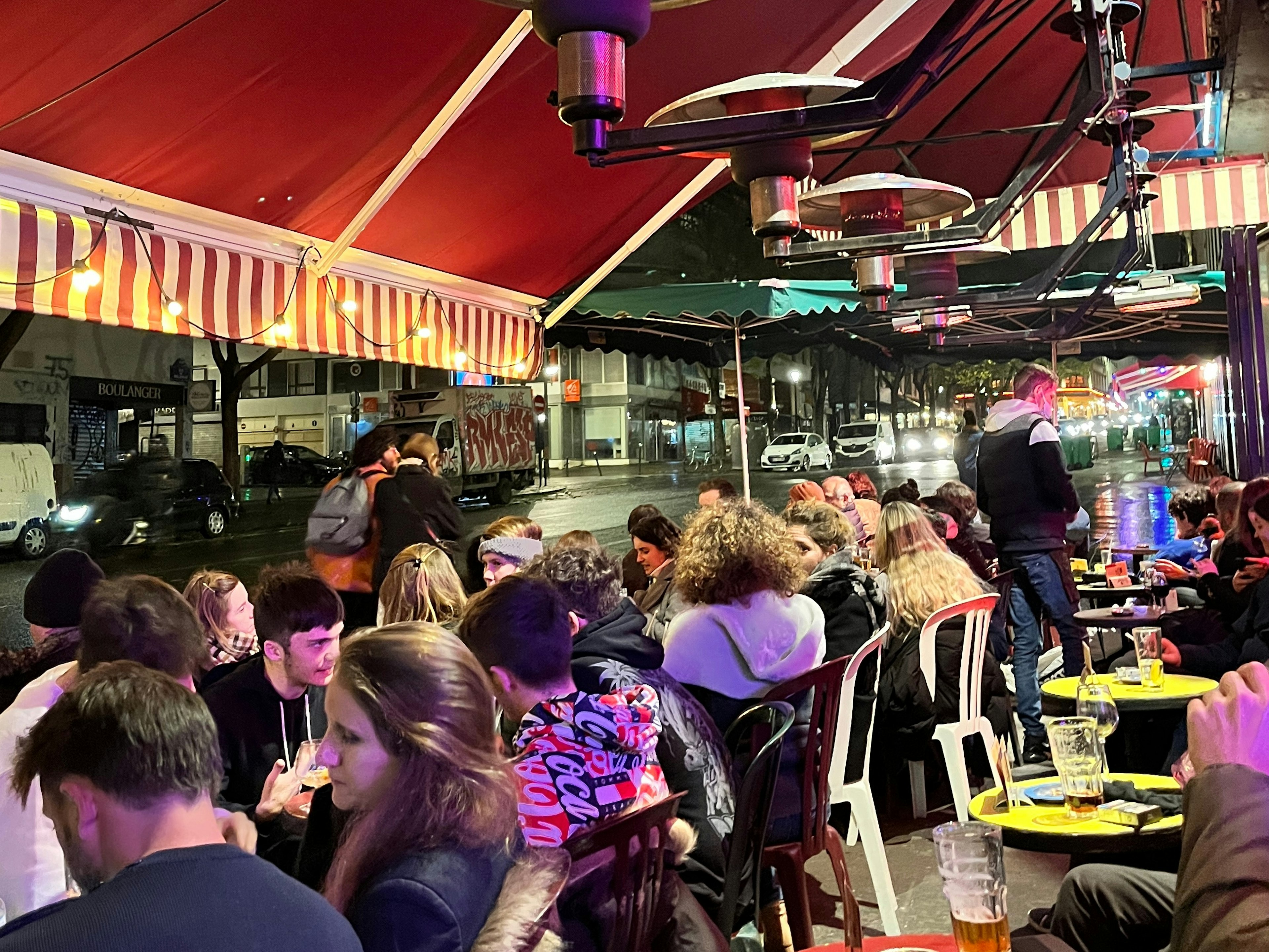 A bar terrace in Paris busy with patrons at night.jpg