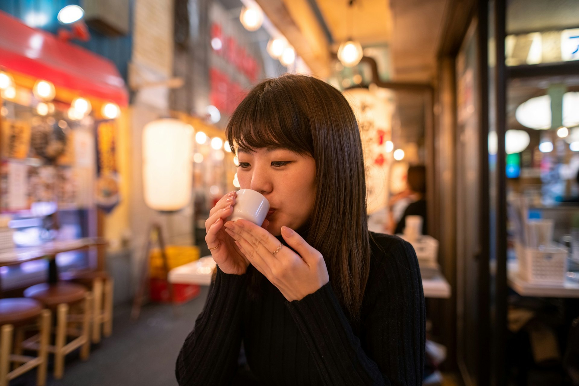 Young woman drinking Japanese 'Saki' rice wine at Izakaya bar