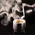 Sake, pouring traditional distilled and fermented alcohol from Japan, served hot. Black background with copy space