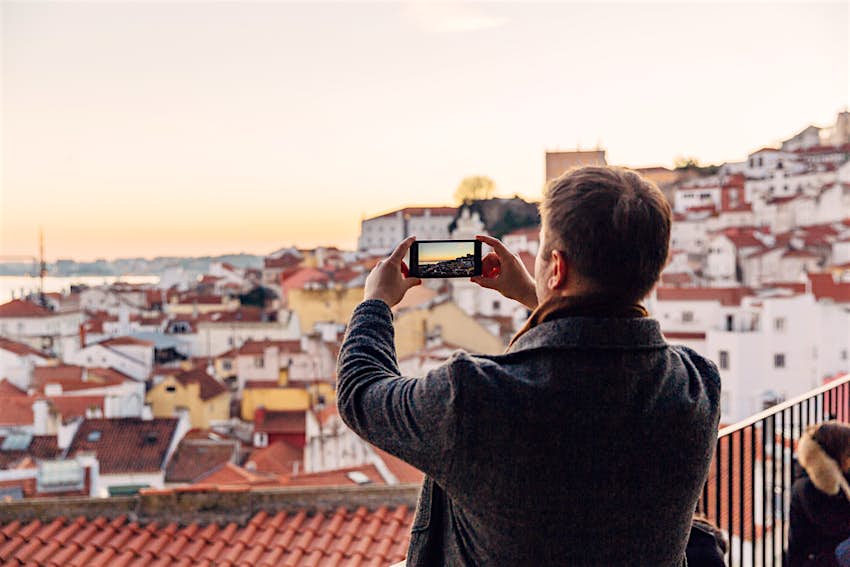 Touriste photographiant les toits de Lisbonne au coucher du soleil à l'aide d'un smartphone, Portugal