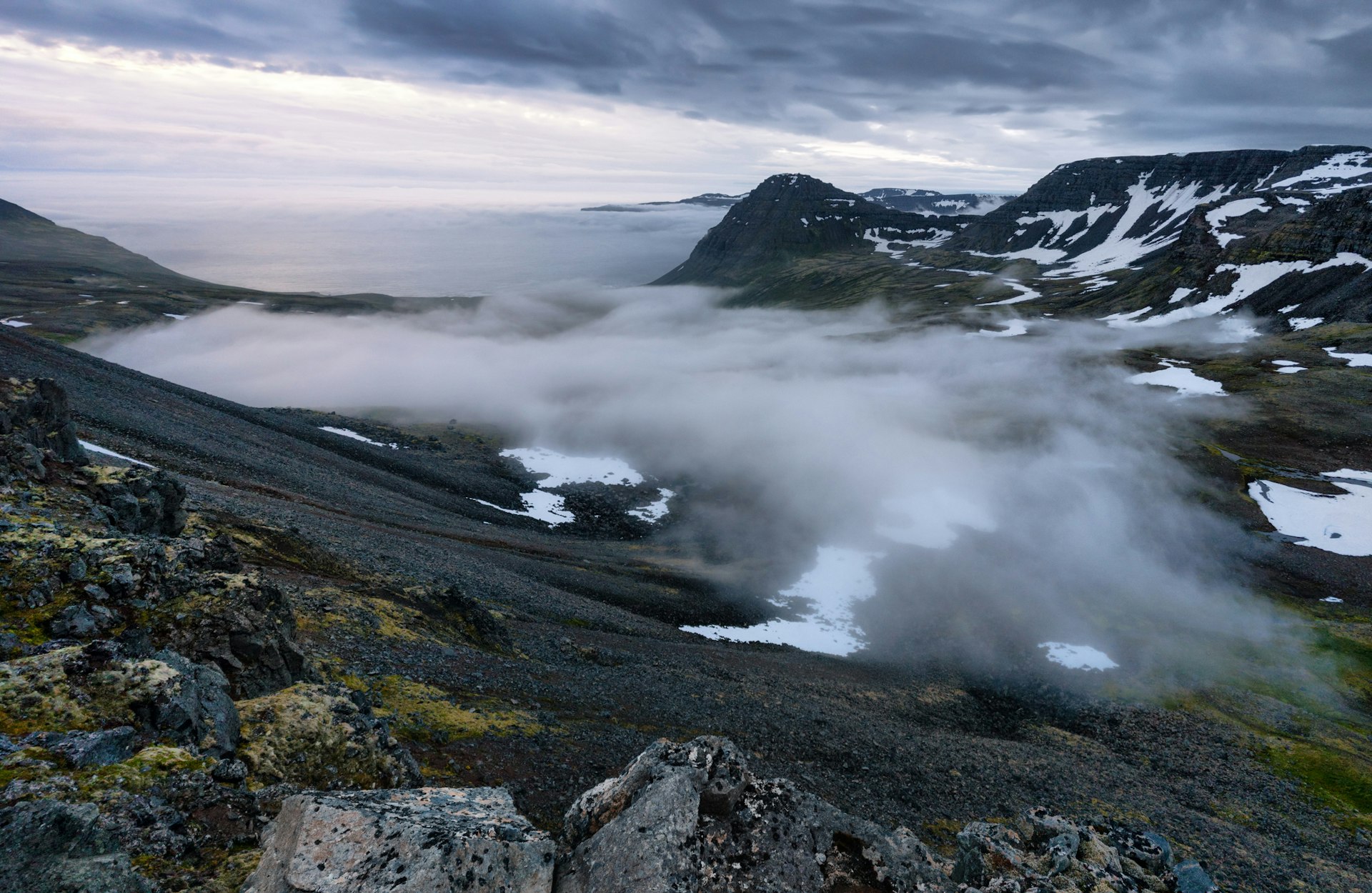 A high-angle view of a cloudy valley surrounded by snowy peaks