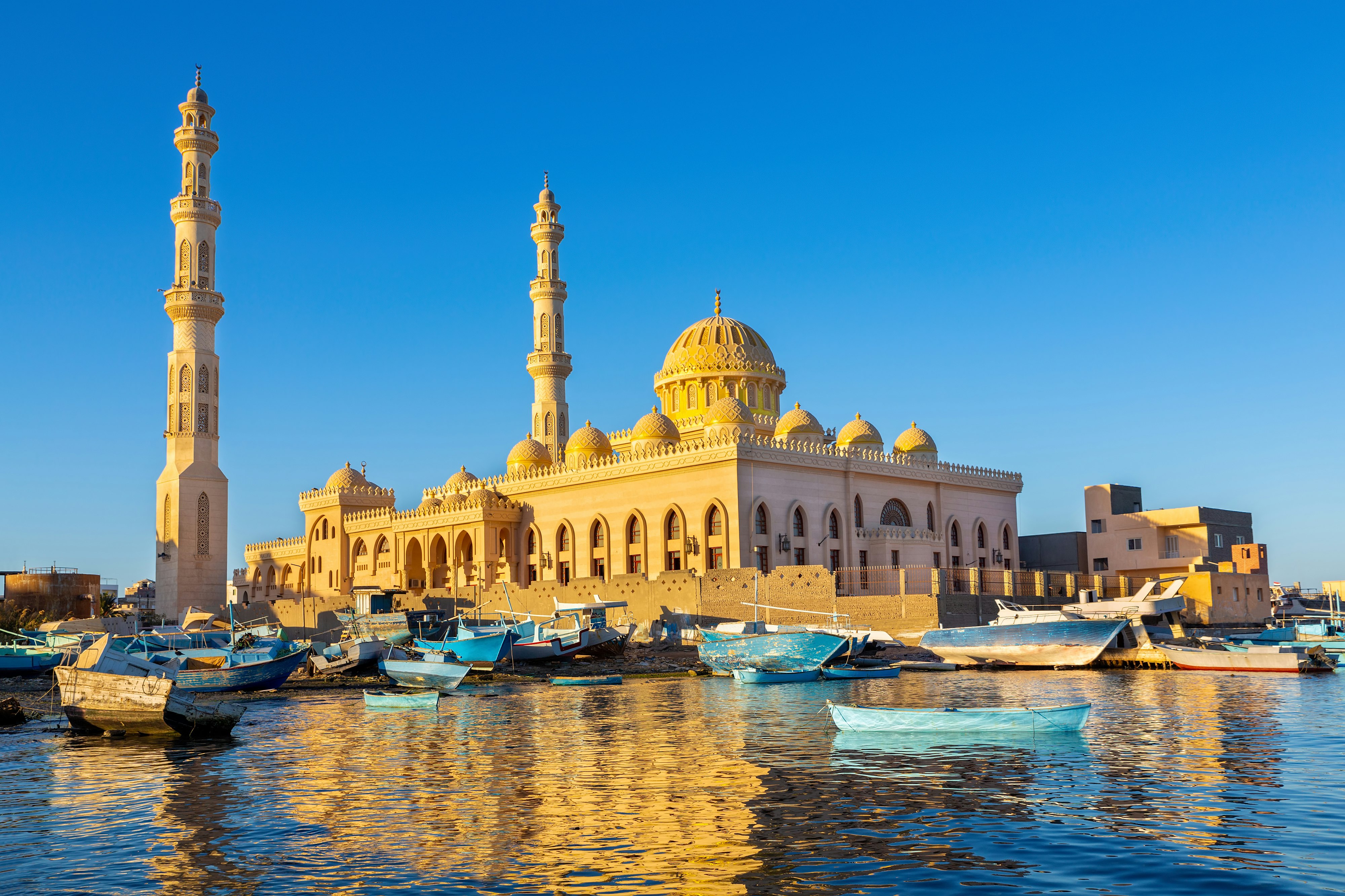 Exterior shot of a mosque. There are a collection of fishing boats moored in the water in front of the mosque.