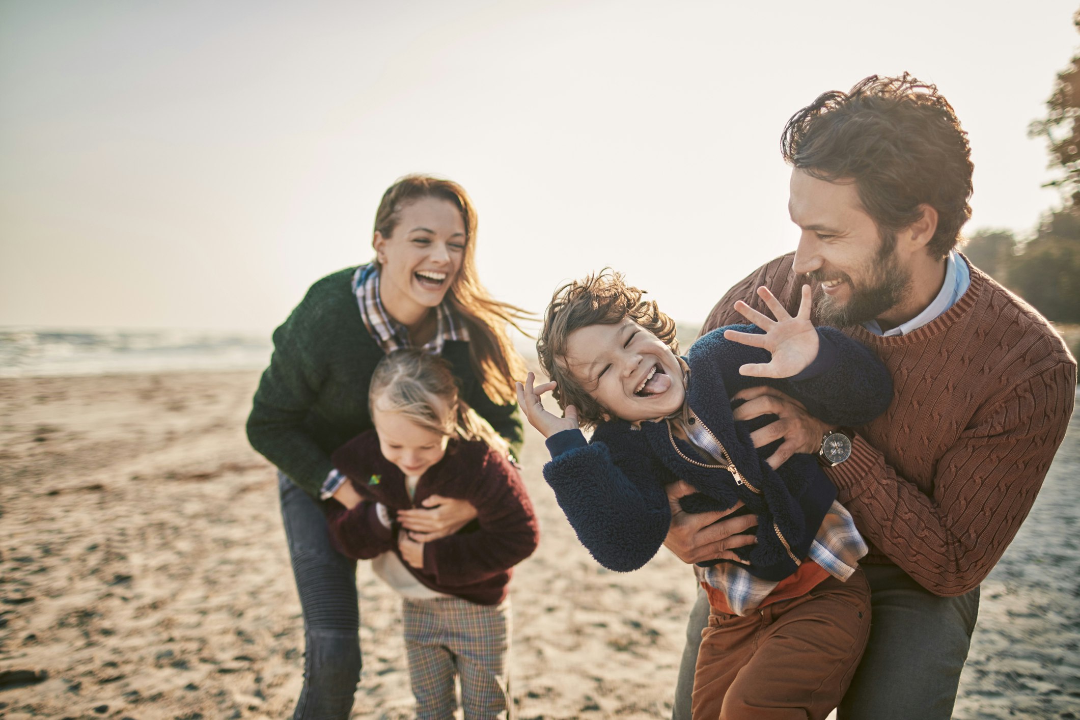 A white family laugh and play on the beach together